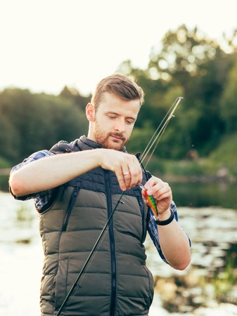 Fisherman with a spinning rod and bait (lure, wobbler)  catching fish in a river. Man on a weekend. Hobby, leisure, active summer and autumn concept. Nature background.の写真素材
