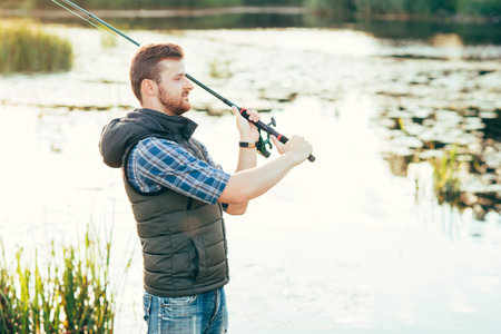 Fisherman with a spinning rod catching fish in a river. Man on a weekend. Hobby, leisure and active...