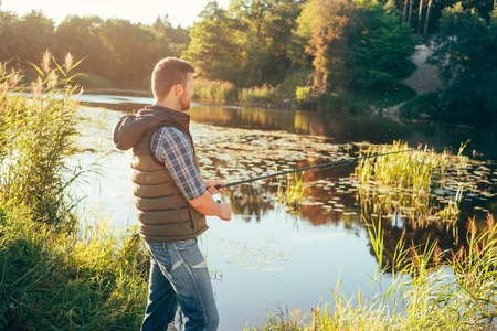 Fisherman with a spinning rod catching fish in a river. Man on a weekend. Hobby, leisure and active summer and autumn concept. Rural background.の写真素材
