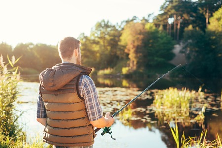 Fisherman with a spinning rod catching fish on a river. Man on a weekend. Hobby, leisure and active summer and autumn concept. Rural background.の写真素材