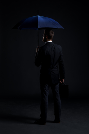 Businessman with a blue umbrella over black background. Business, protection and crisis concept.の写真素材