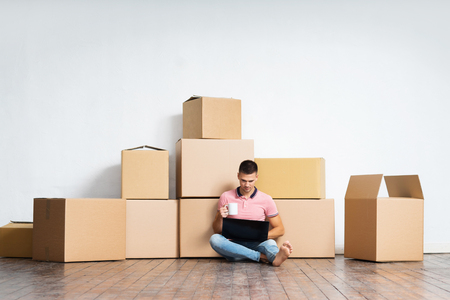 Young man moving to a new home. Handsome guy with notebook laptop computer and boxes.の写真素材