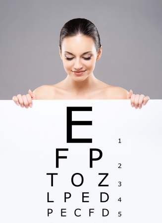 Attractive woman with a banner of test vision table over grey background.の写真素材