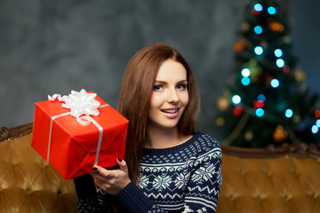 Close-up of beautiful woman with a Christmas present. Young girl celebrating xmas. Tree on a background. Holidays, winter and celebration concept.の写真素材