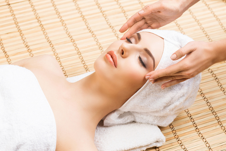 Beautiful, young and healthy woman on bamboo mat in spa salon having face massage. Spa, health and healing concept.の写真素材
