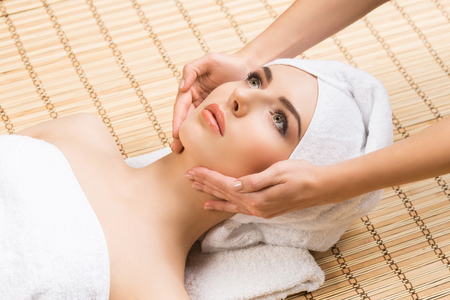 Beautiful, young and healthy woman on bamboo mat in spa salon having face massage. Spa, health and healing concept.の写真素材