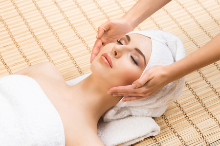 Beautiful, young and healthy woman on bamboo mat in spa salon having face massage. Spa, health and healing concept.の写真素材