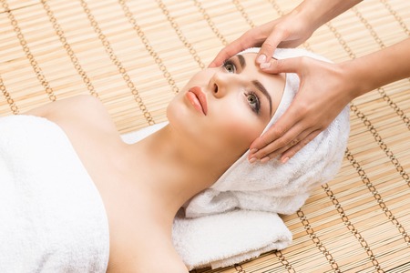 Beautiful, young and healthy woman on bamboo mat in spa salon having face massage. Spa, health and healing concept.の写真素材