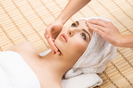 Beautiful, young and healthy woman on bamboo mat in spa salon having face massage. Spa, health and healing concept.の写真素材
