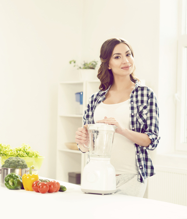 Beautiful pregnant woman preparing breakfast in kitchen. Motherhood, pregnancy, maternity concept.の写真素材