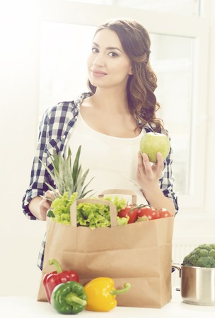 Beautiful pregnant woman with shopping bags in kitchen. Motherhood, pregnancy, maternity concept.の写真素材