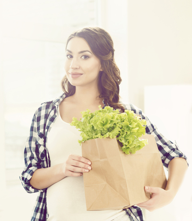 Beautiful pregnant woman with shopping bags in kitchen. Motherhood, pregnancy, maternity concept.の写真素材