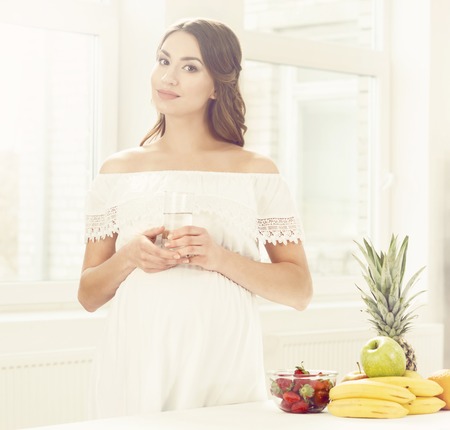 Beautiful pregnant woman with fruits in kitchen. Motherhood, pregnancy, maternity concept.の写真素材