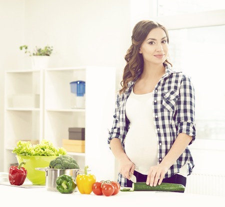 Beautiful pregnant woman preparing breakfast in kitchen. Motherhood, pregnancy, maternity concept.の写真素材
