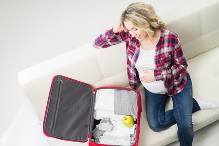 Young attractive pregnant woman packing children's wear to go to maternity clinic.の写真素材