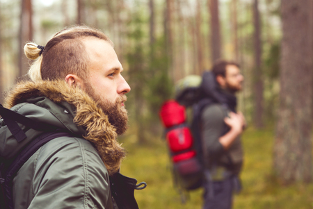 Camp, adventure, traveling and friendship concept. Man with a backpack and beard and his friend hiking in forest. Autumn color and hipster filter.の写真素材