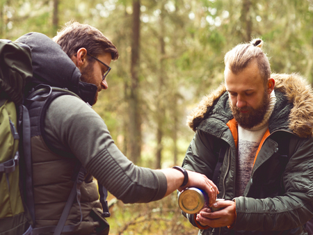Camp, adventure, traveling and friendship concept. Man with a backpack and beard and his friend hiking in forest. Autumn color and hipster filter.の写真素材