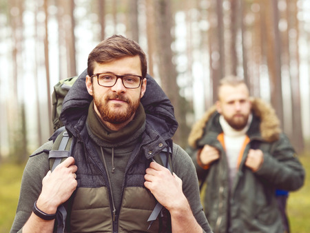Camp, adventure, traveling and friendship concept. Man with a backpack and beard and his friend hiking in forest. Autumn color and hipster filter.の写真素材