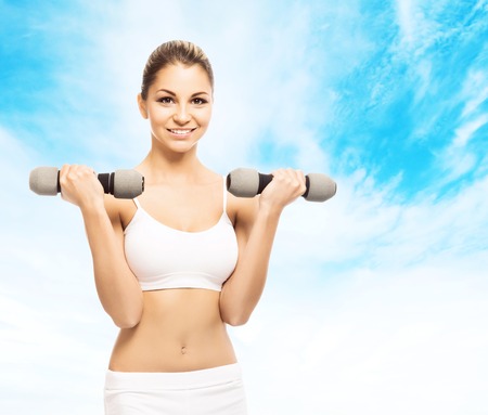 Sporty, athletic and attractive woman with a dumbbells over heaven background. Sport, dieting and healthy lifestyle concept.の写真素材