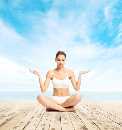 Young, sporty and beautiful girl meditating on a pier at summer. Yoga concept.の写真素材