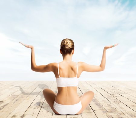 Beautiful woman with a perfect body meditating on a pier. Yoga, sport and summer concept.の写真素材