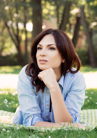 Portrait of gorgeous brunette leaning on her hand and thinking of something in the parkの写真素材