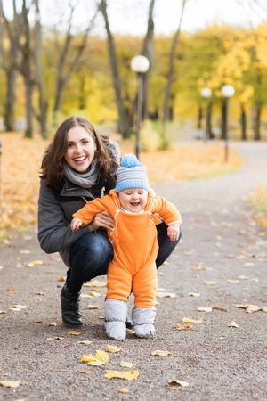 Mother teaching her toddler son to walk in the park. Autumn nature background. Love and family concept.の写真素材