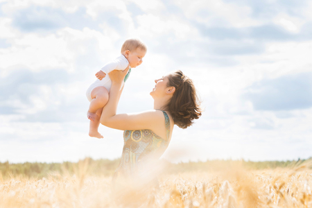 Young and beautiful woman playing with her infant baby in a meadow of wheat. Summer concept.の写真素材