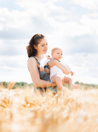 Young and beautiful woman playing with her infant baby in a meadow of wheat. Summer concept.の写真素材
