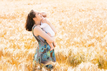 Young and beautiful woman playing with her infant baby in a meadow of wheat. Summer concept.の写真素材