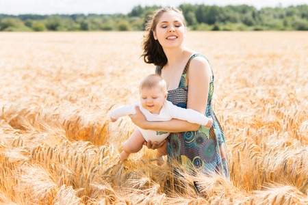 Young and beautiful woman playing with her infant baby in a meadow of wheat. Summer concept.の写真素材