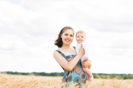 Young and beautiful woman playing with her infant baby in a meadow of wheat. Summer concept.の写真素材