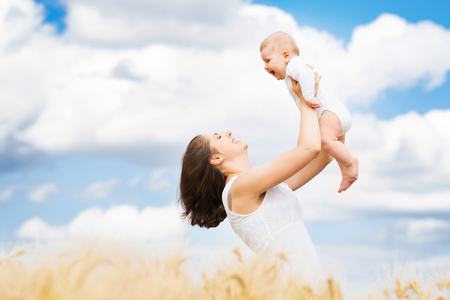 Young and beautiful woman playing with her infant baby in a meadow of wheat. Summer concept.の写真素材