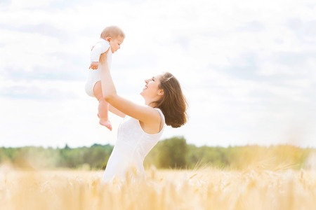 Young and beautiful woman playing with her infant baby in a meadow of wheat. Summer concept.の写真素材