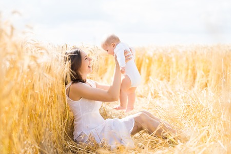 Young and beautiful woman playing with her infant baby in a meadow of wheat. Summer concept.の写真素材