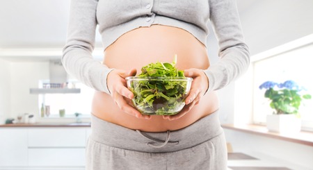 Woman expecting a baby. Pregnant belly closeup. Kitchen with window.の写真素材