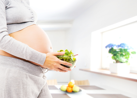 Woman expecting a baby. Pregnant belly close-up. Kitchen with window.の写真素材