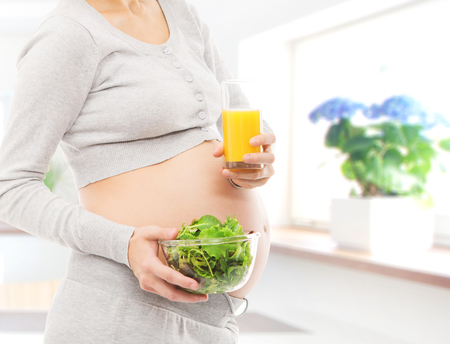 Woman expecting a baby. Pregnant belly closeup. Kitchen with window.の写真素材