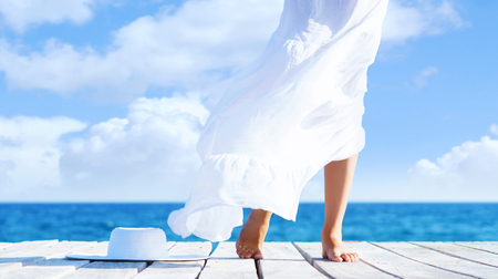 Beautiful and healthy female legs in white skirt on a wooden pier. Vacation, resort and traveling concept.の写真素材