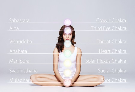 Woman meditating in lotus position. Colored chakra lights over her body. Yoga, zen, Buddhism, recovery and wellbeing concept.の写真素材