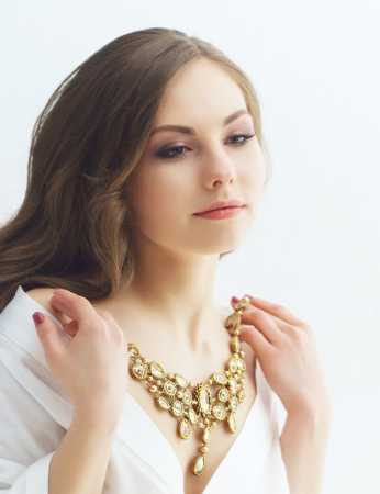 Beauty portrait of attractive and young woman trying golden necklace.の写真素材