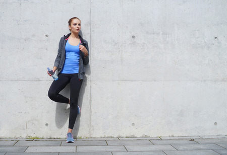 Young, fit and sporty woman standing in front of concrete cement wall. Fitness, sport, urban jogging and healthy lifestyle concept.の写真素材