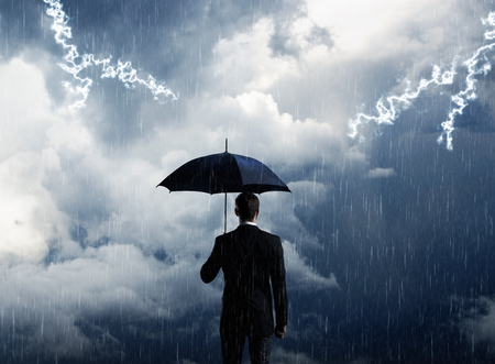 Businessman with umbrella standing over stormy background.の写真素材
