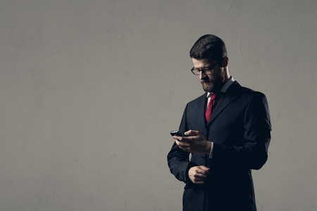 Businessman with smartphone standing over white wall.の写真素材