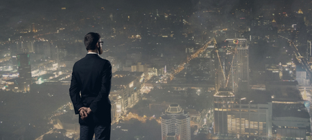 Businessman standing over night city background.の写真素材