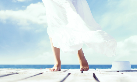 Beautiful feet of a woman in white dress on a wooden pier. Sea and sky background.の写真素材