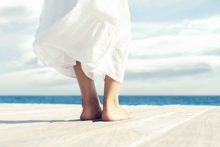 Beautiful feet of a woman in white dress on a wooden pier. Sea and sky background.の写真素材