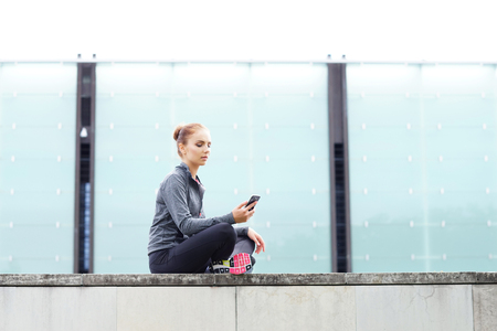 Young, fit and sporty woman sitting on a concrete border. Fitness, sport, urban jogging and healthy lifestyle concept.の写真素材