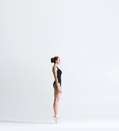 Ballerina in point shoes and bodysuit is dancing in studio. Young and graceful female ballet dancer.の写真素材