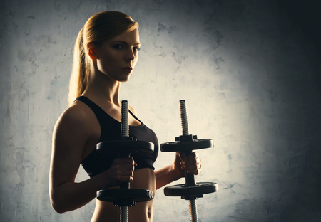 Fit body of beautiful, healthy and sporty woman with a dumbbells. Slim woman posing in sportswear.の写真素材